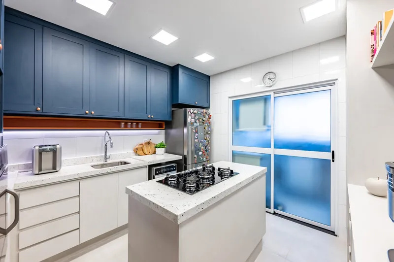 Cozinha planejada com armários azuis e bancada em granito branco — reforma residencial Santos